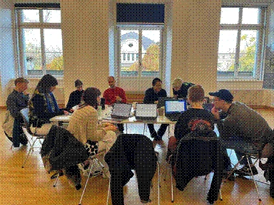 The room is large with big windows and a big table in the middle. During the workshop, a group of nine people sit in front of their computers.